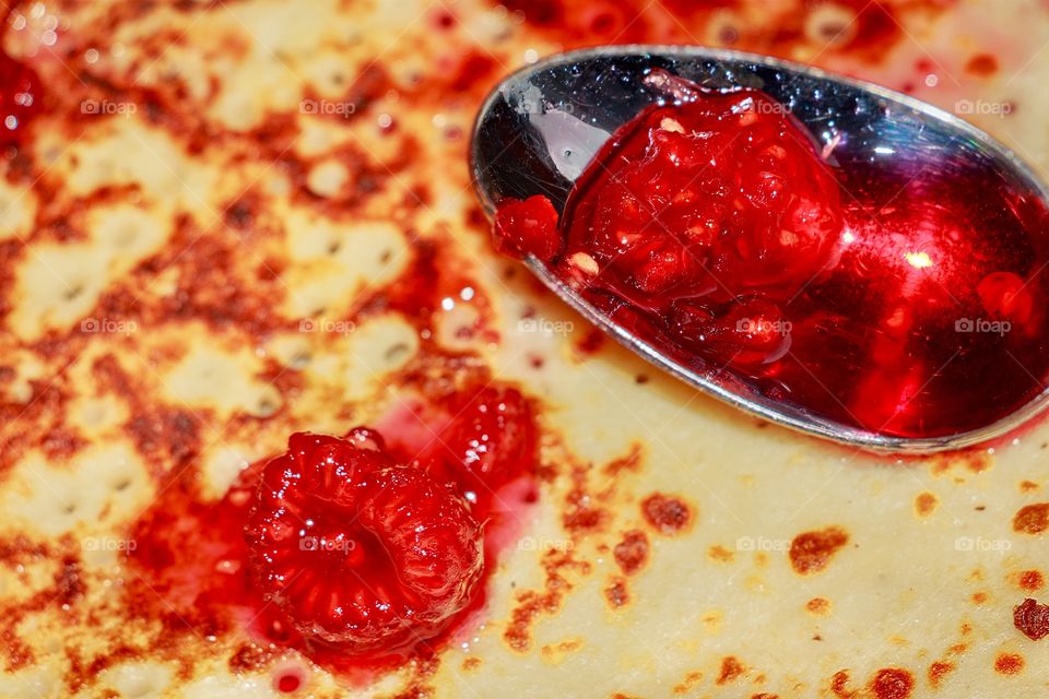 Macro of spoon full with raspberry jam in a pancake