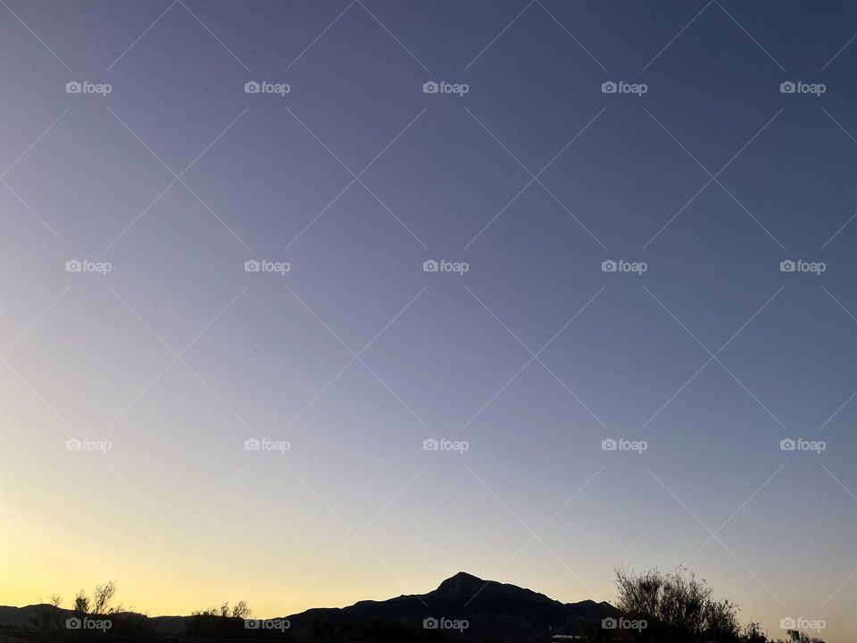 A yellow sunset with mountains and trees. 