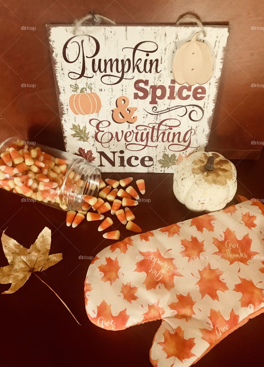 Pumpkin spice and everything nice fall greeting sign and display. Delicious candy corn, pumpkin, golden leaf and oven mitt displayed. Getting ready for the autumn season. 
