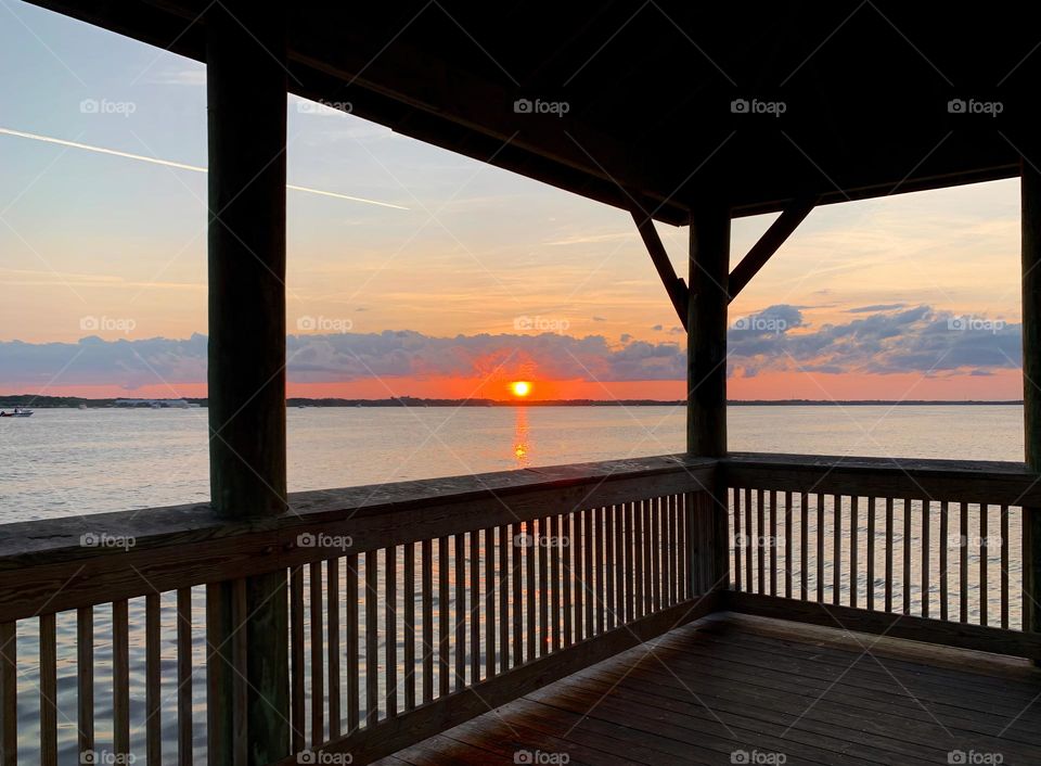 Sunset In The Horizon With Deep Orange Color Sighting From Gazebo On The Dock By The Island Reflecting On The Water.