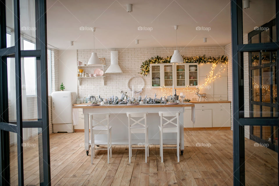 Festive winter cozy kitchen interior with garlands, decorations and gifts.  Christmas dinner at the decorated table.