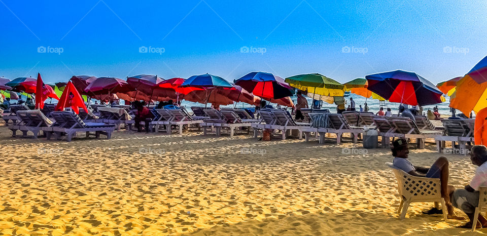 Colourful umbrella with seating chairs on beach sand having colourful surrounding.