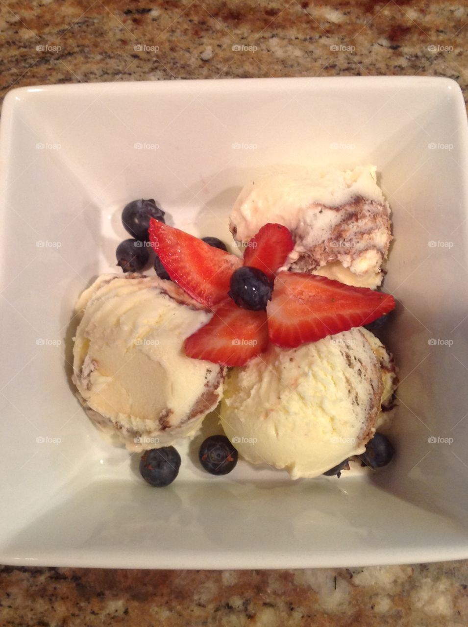 A photo of Vanilla ice cream with strawberries and blueberries. 