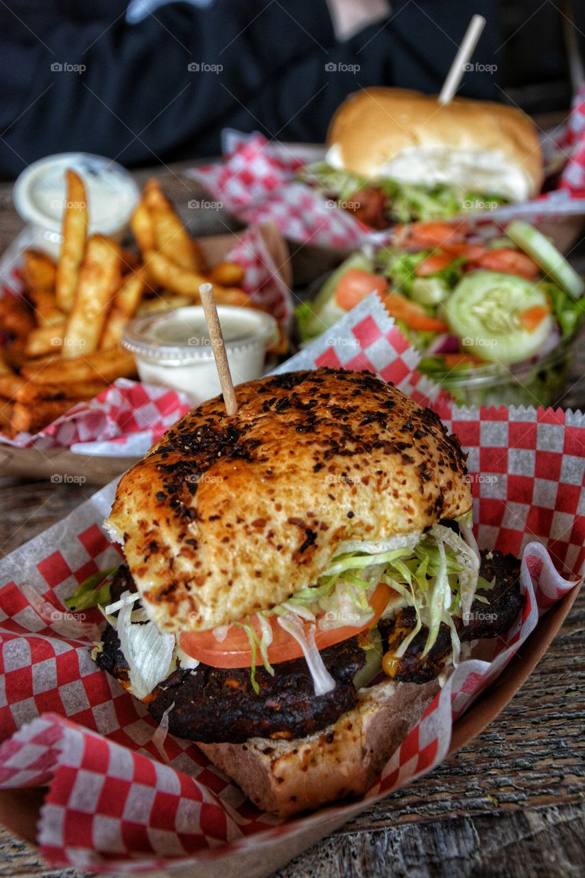 Hamburger with shredded lettuce tomato with a side of French fries and salad.