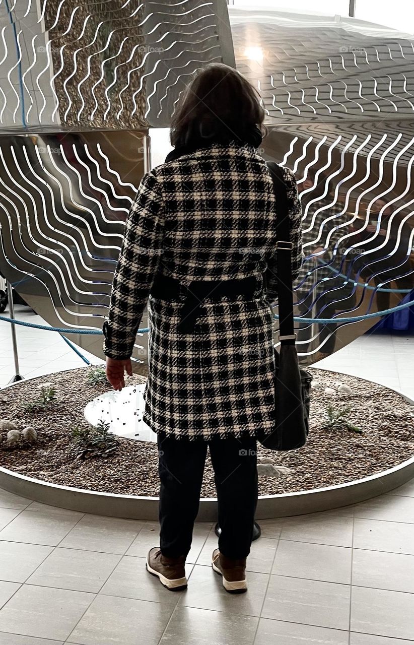 A woman is looking at a work of art wearing a checkered jacket.
