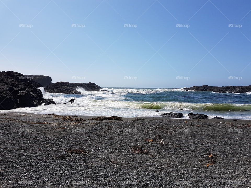 bright sunny clear sky summer day outside, sandy beach with rocks and white cap waves of the blue ocean in Tofino, Canada