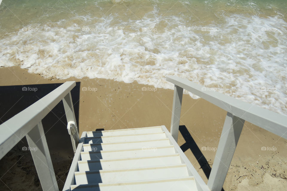 Wooden staircase to a Mediterranean beach. Wooden stairs walkway leading to a sandy beach on a summer day.