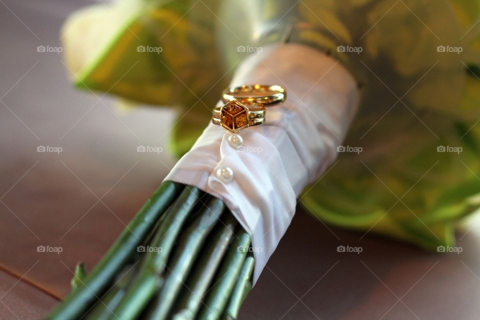 A bride and groom's wedding rings resting on a bouquet stem