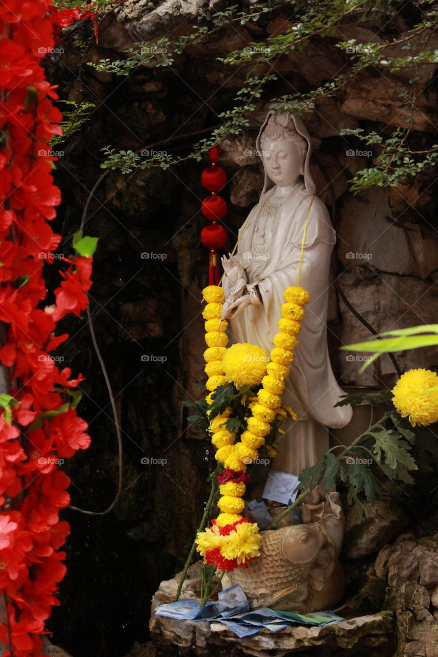 Red petals and yellow flowers covering beautiful statue