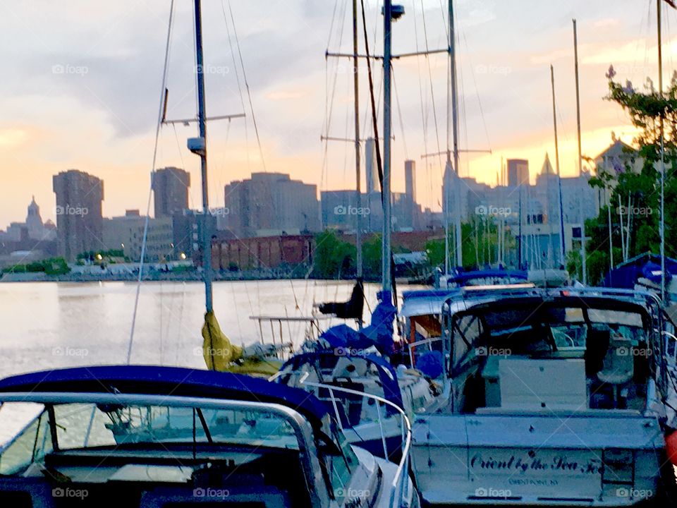 Sailboats in the East River at Newtown Creek in LIC, Queens, NY at dusk. The sun has almost set completely. The sky and the sea reflect its last golden rays. In the distance you can see the cityscape of Queens and beyond. 2018 Hypnotic Productions