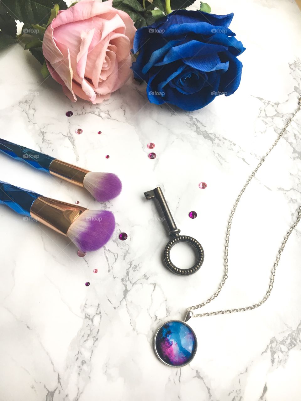 Makeup brush flat lay on a marble background with roses and jewelery.