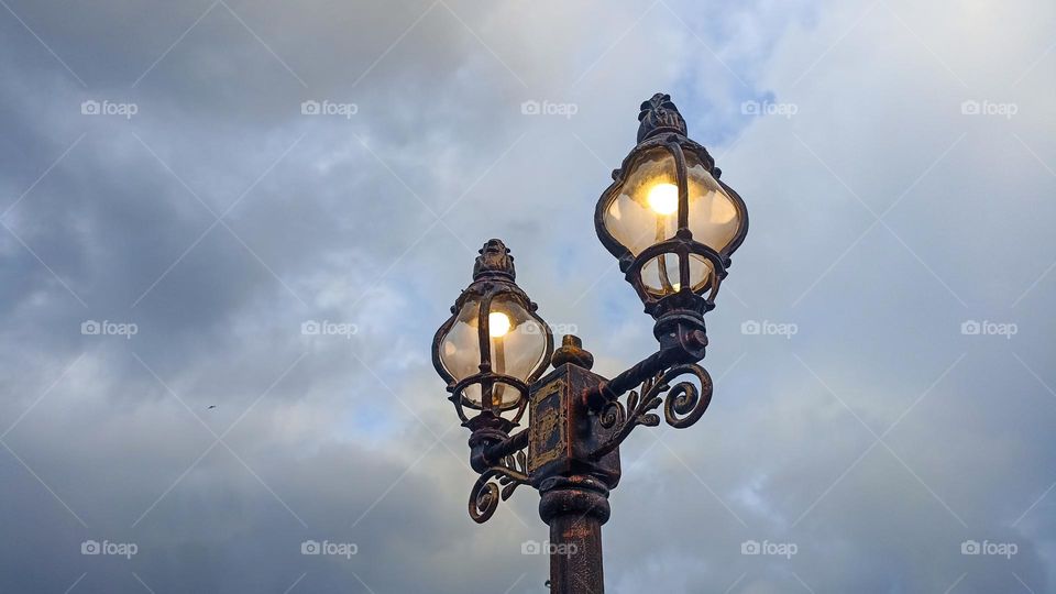 Low angle view of illuminated street light against cloudy sky