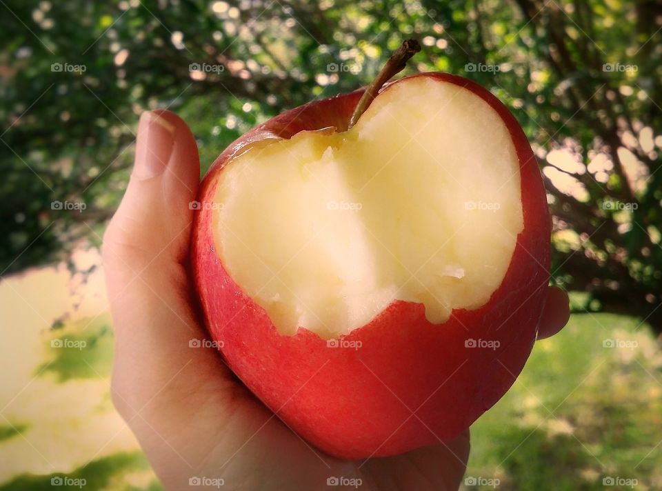 Staying in good shape an apple a day does keep the doctor away a woman's hand holding an apple with two bites out of it outside in summer