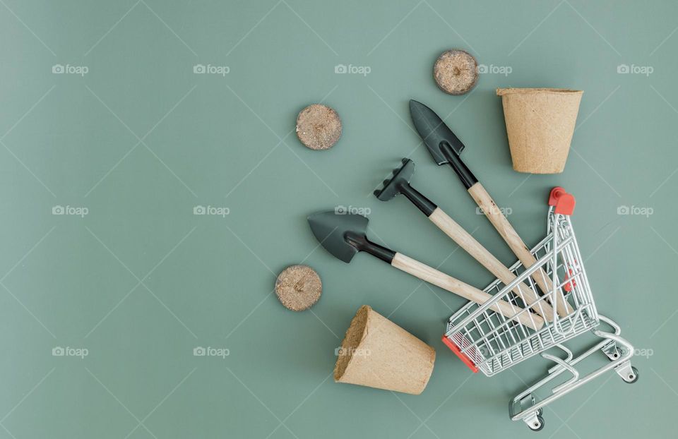 Three gardening tools with cardboard glasses spilling out of a shopping cart lie against a natural green background with copy space on the left, flat lay close-up.