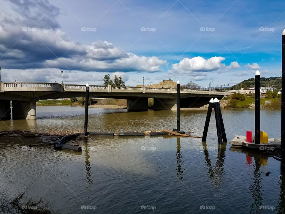 Waters rising on the Napa Valley river in downtown Napa California, clouds in the sky above a bridge 