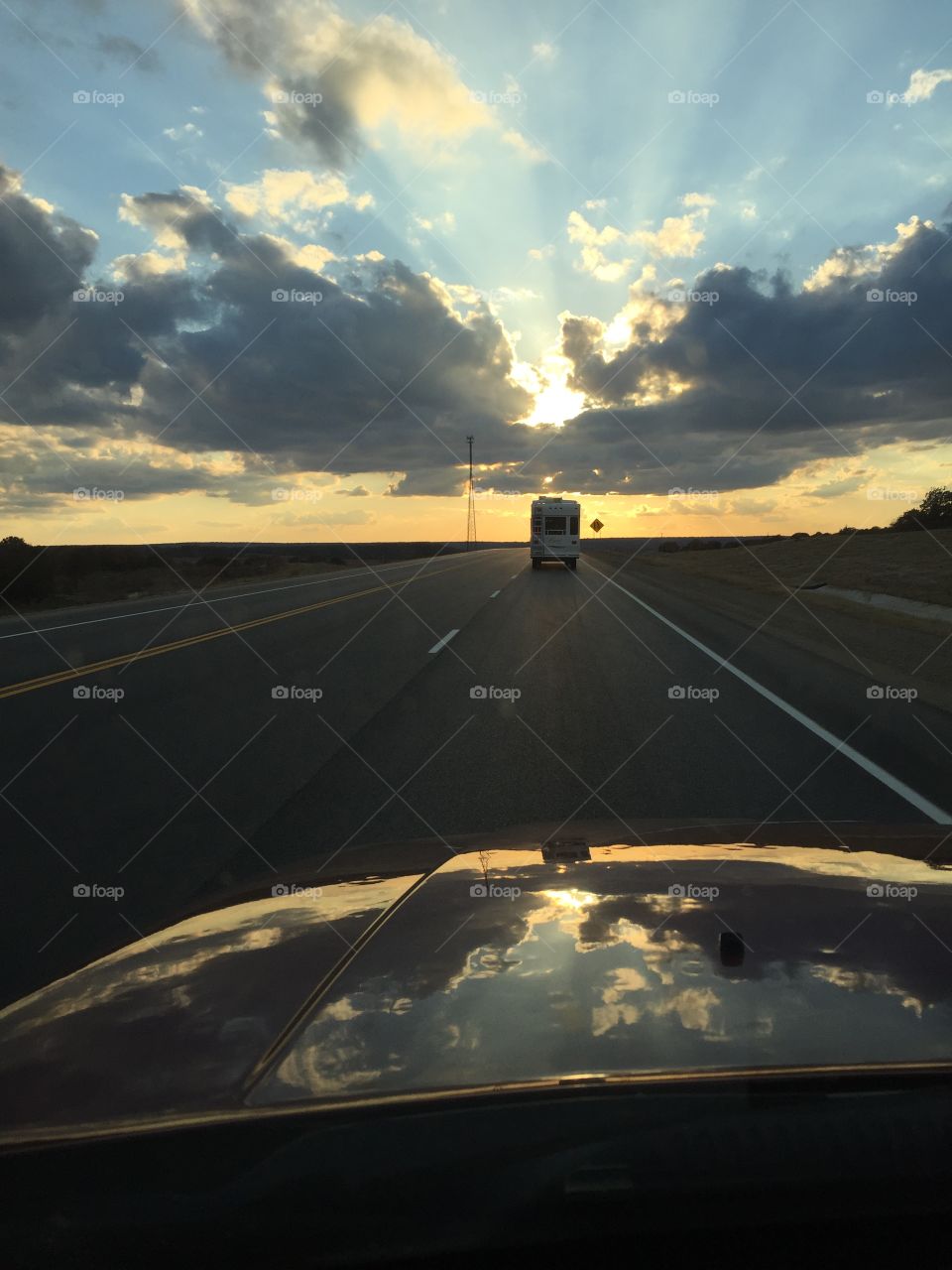 Traveling down the road at sunset on the next adventure following an RV on open highways. The sky welcomes what comes next. 