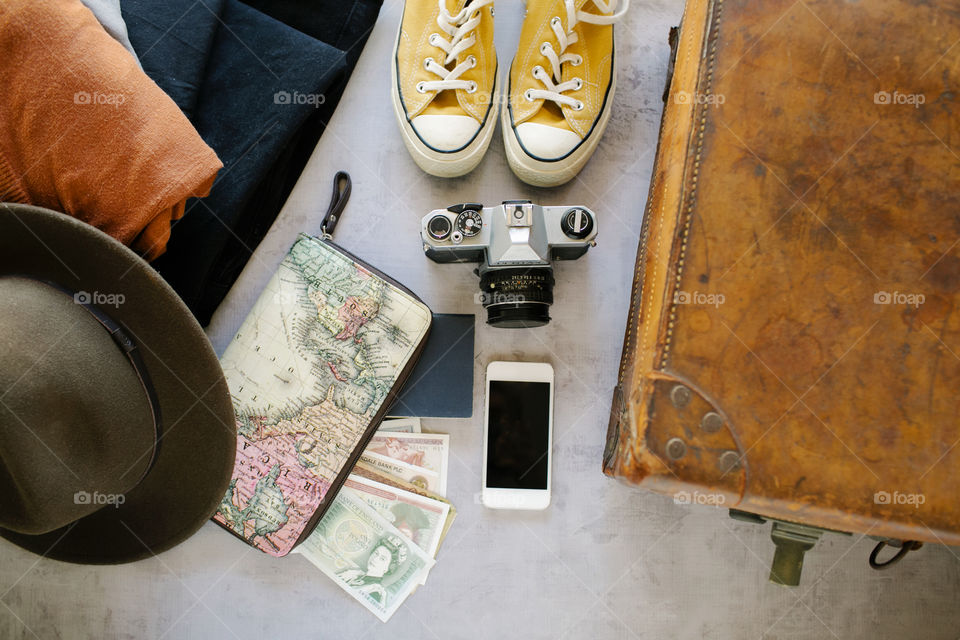 Adventure flat lay with vintage suitcase, smartphone, camera, money, passport, sneakers, hat and clothes 