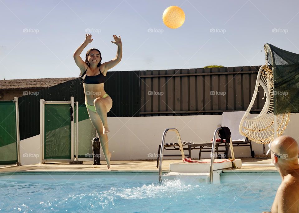 A young woman leaps to get a ball while jumping in the pool