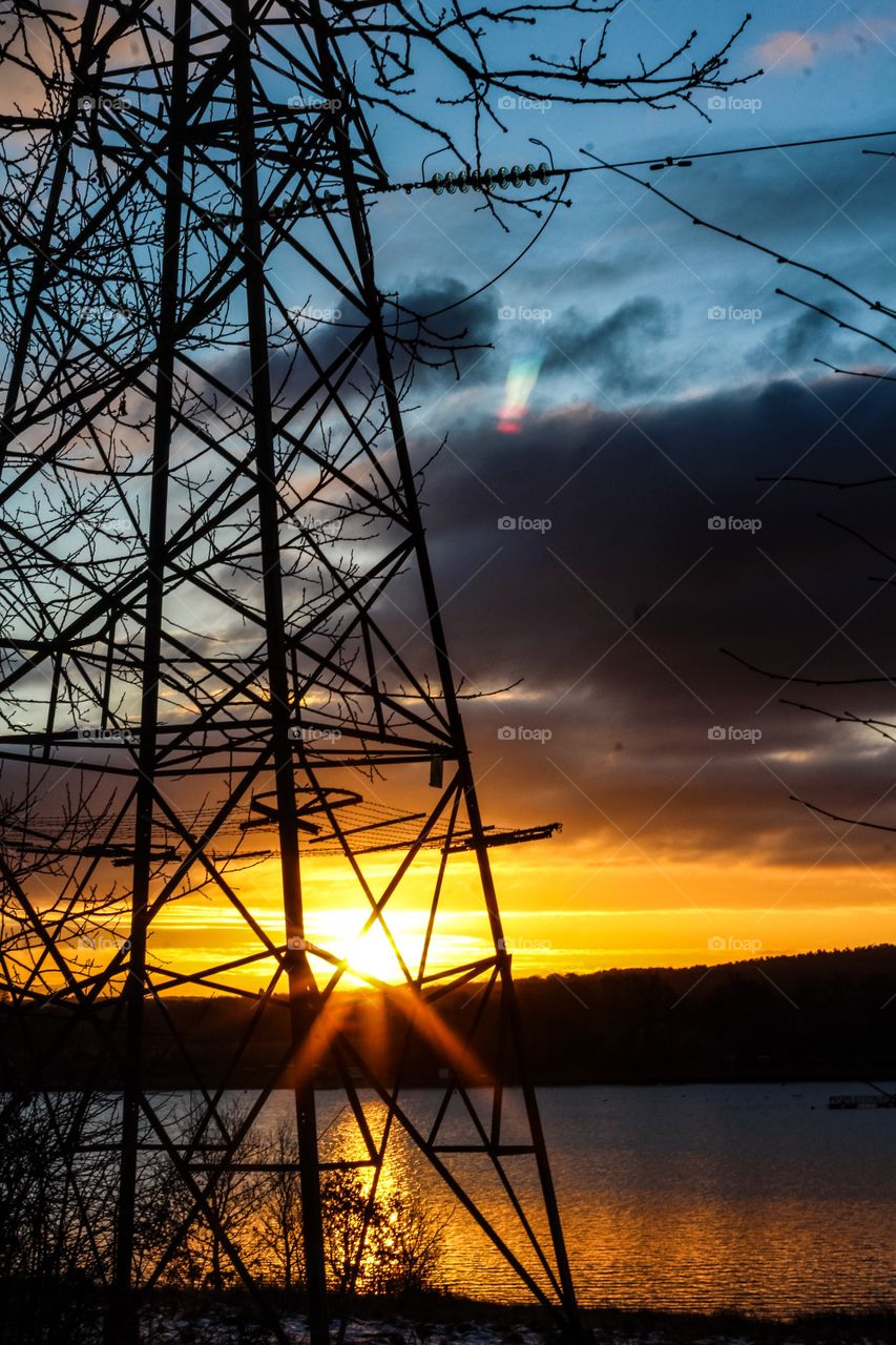 Electricity pylon near lake during sunset