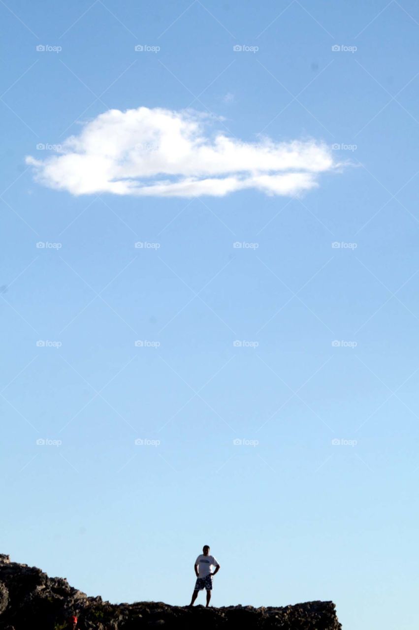 Under the cloud . Italian man standing on the rocks under a single cloud in the blue sky. Taken in Cetraro, Calabria, Southern Italy.