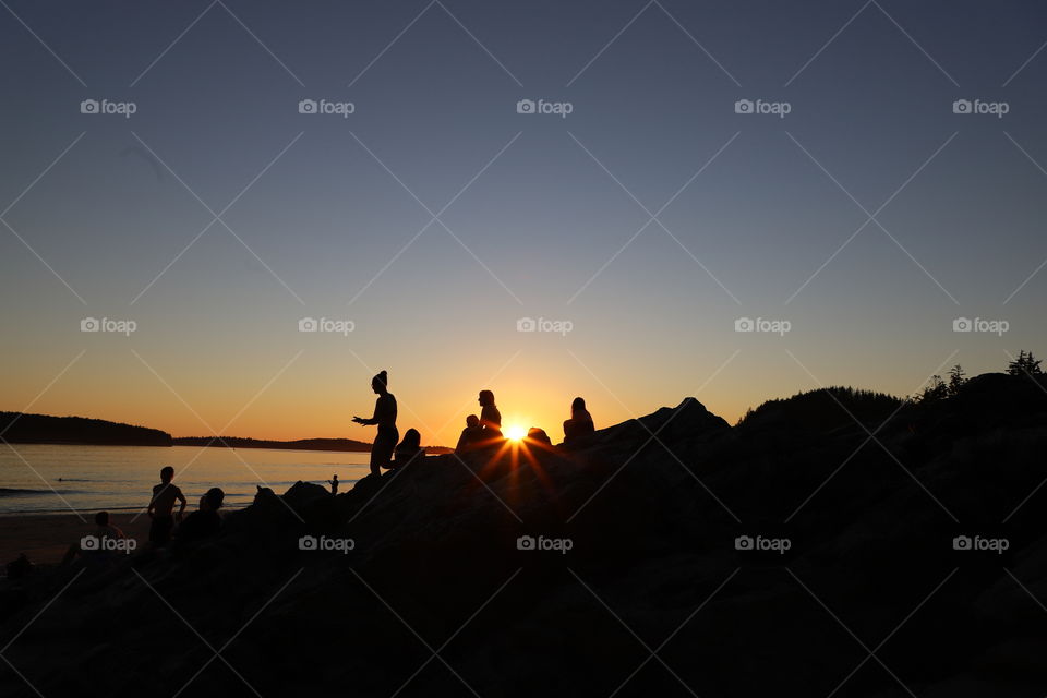 Sun is setting down on beach while young people are gathered for some summer fun 