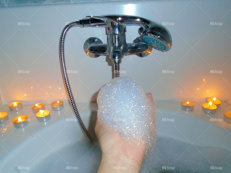 Hand of woman holding foam while taking a bubble bath surrounded by candles and a glass of Coca Cola