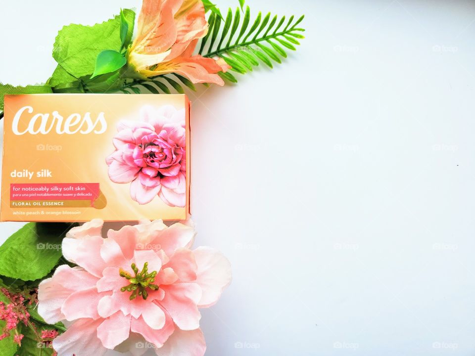 Left side oriented:  the new look single pack daily silk Caress bar surrounded by two simple florals on a white background.