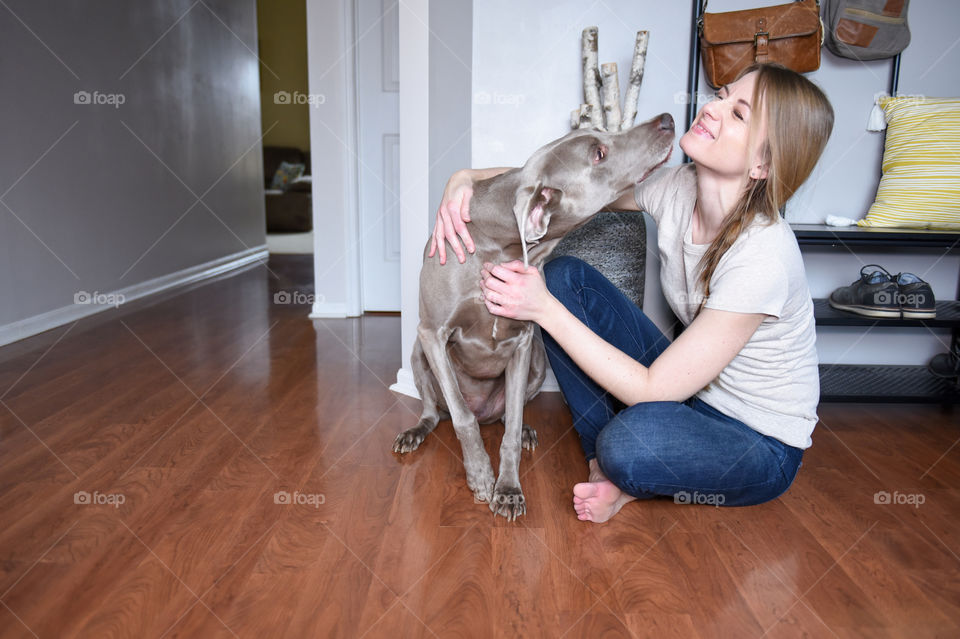 Woman playing with her weimaraner dog on the floor indoors