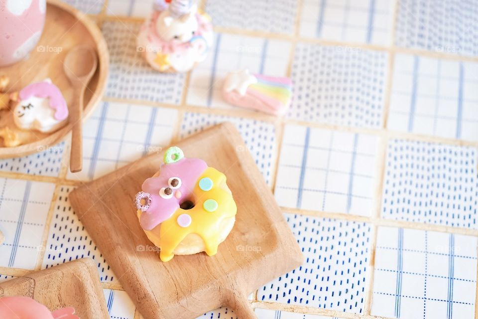 Cute donut. A cute monster sugar glazed doughnut served on a wooden table, soft focus. Fancy food concept for birthday or creative party.