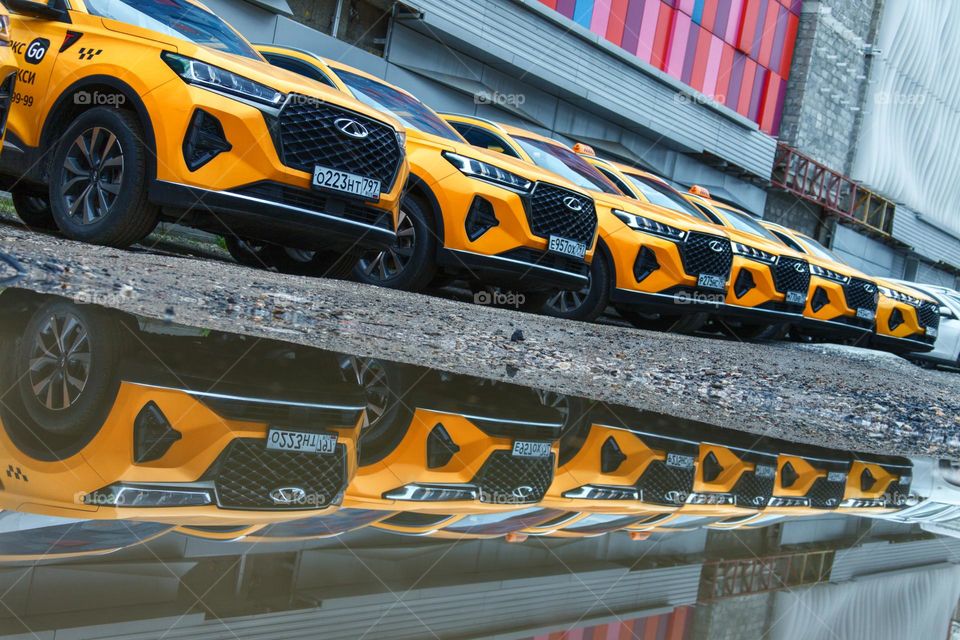 Orange taxi cars stand in a row and are reflected in a puddle