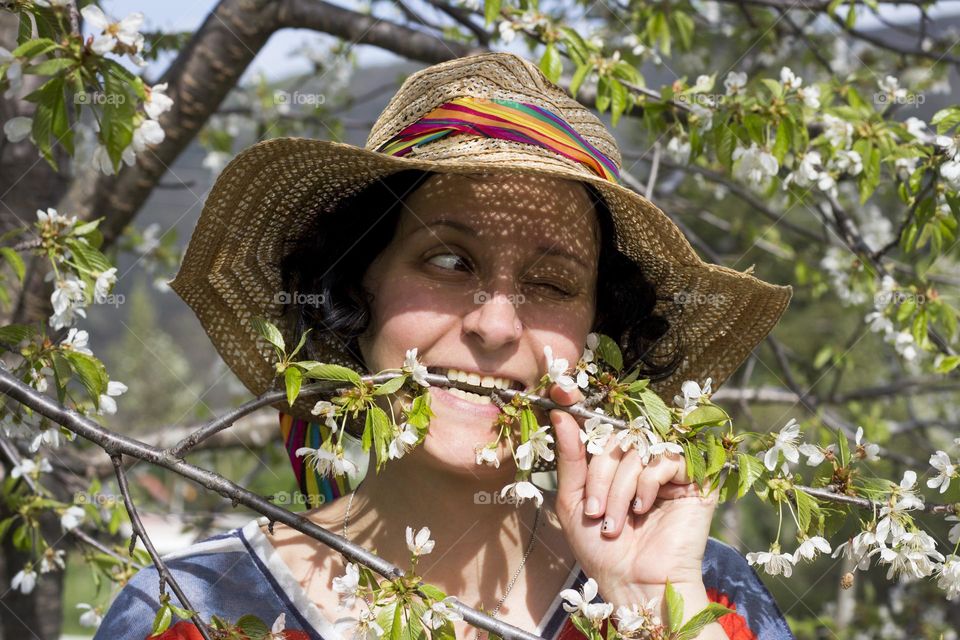 Woman bite a branch of blooming cherry tree, funny portrait in the garden