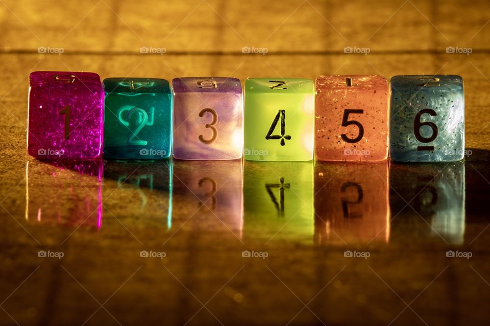 A row of colorful translucent dice with beautiful reflections on a shiny surface. 