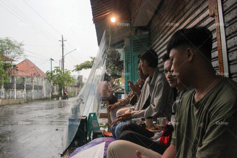 Semarang, Central Java, Indonesia - December 13, 2023: A group of teenagers are gathering in a coffee shop on a rainy day