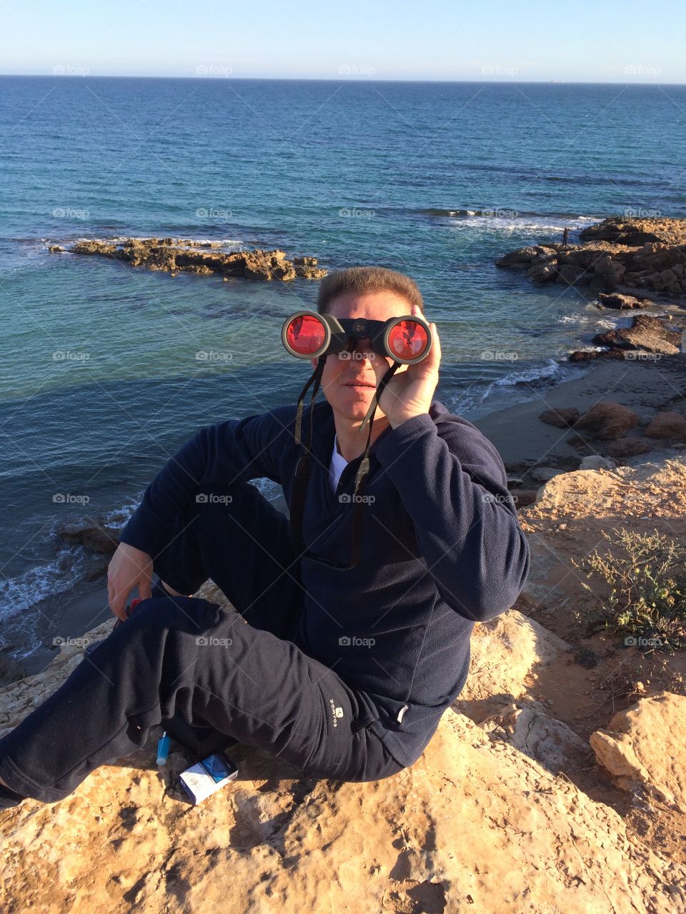 A man watching in binoculars on the rocky beach