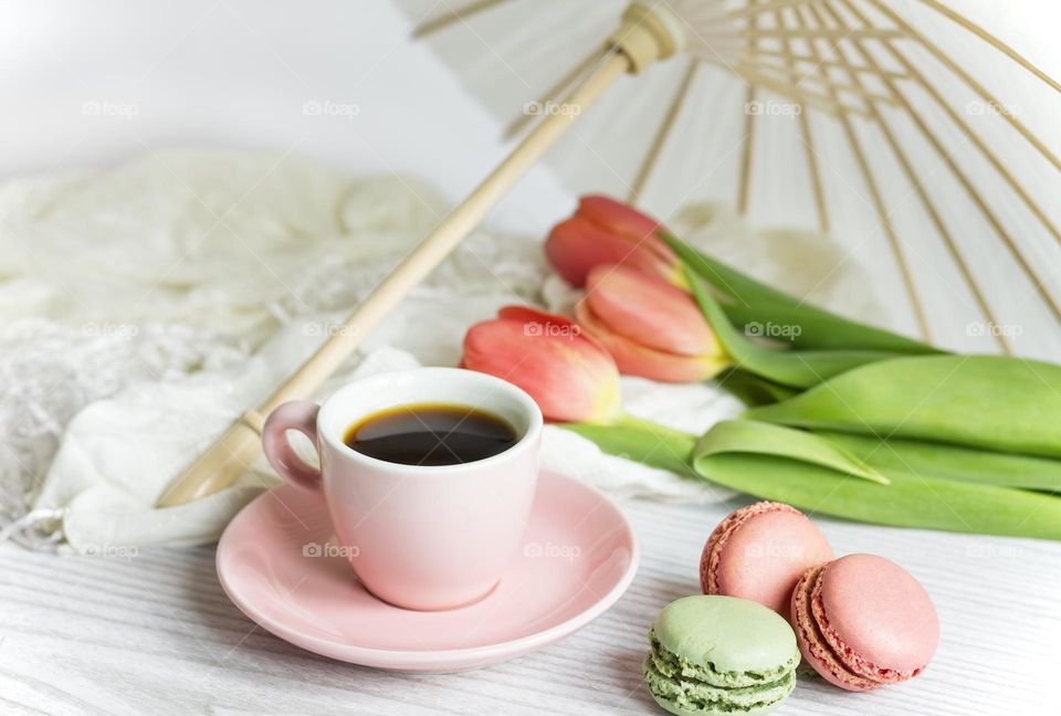 Coffee in a pink cup and saucer with macaroons and tulips under a white paper parasol