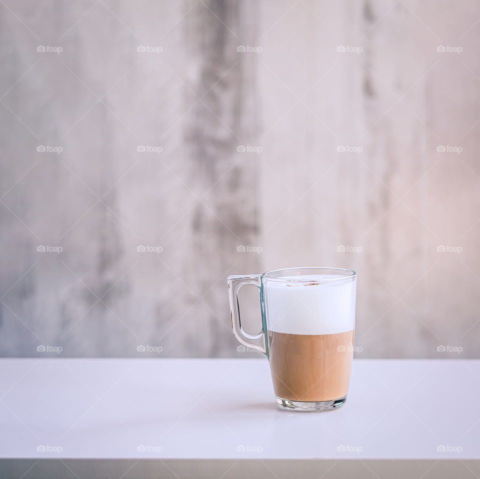 Coffee with milk foam in the glasses cup at the table.