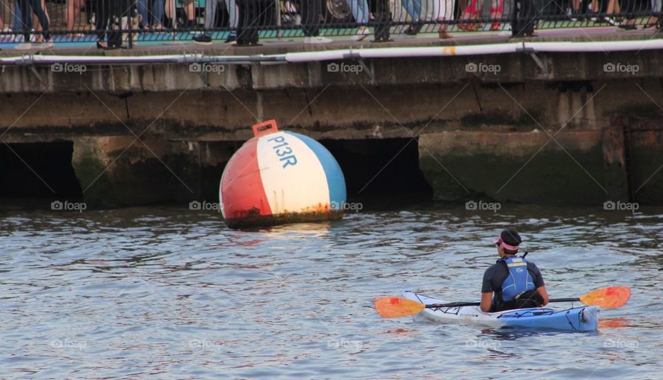 Man in blue life vest paddles bright blue canoe on Hudson River on May evening