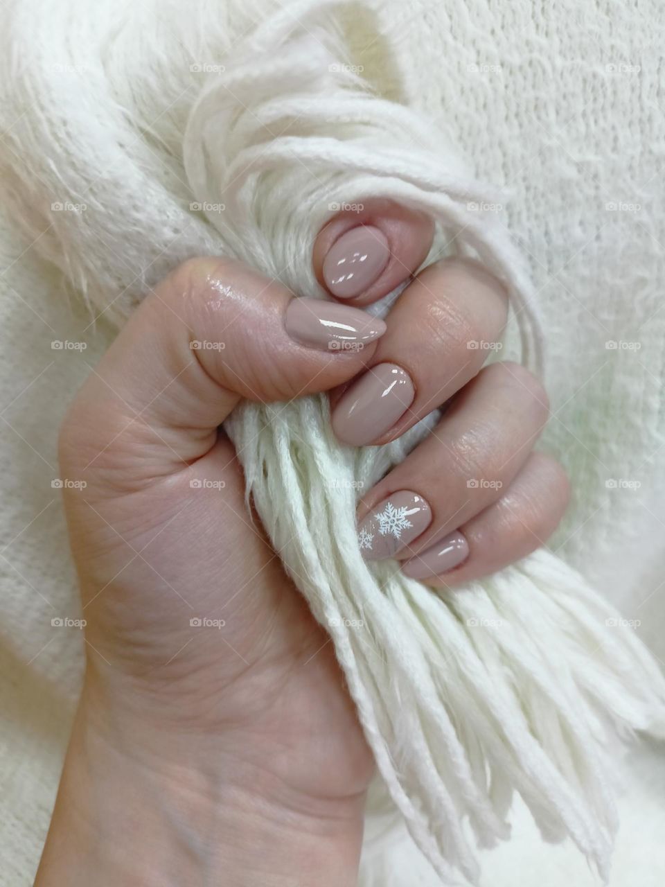 manicure on a female hand, the color of nails is coffee with milk, a white snowflake, female hands on a white background, a warm fluffy scarf, nail polish