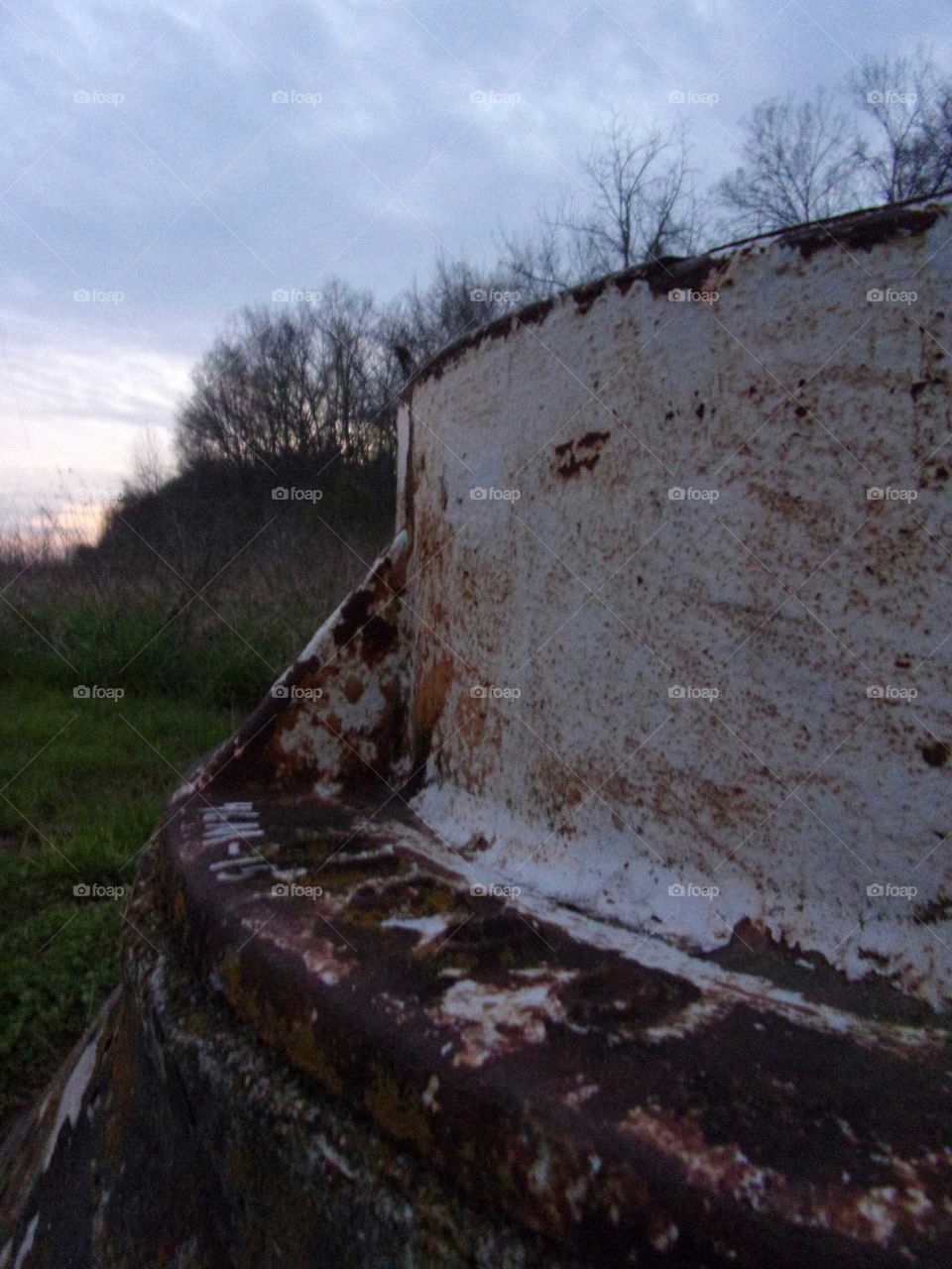 Rusty sewage access in the middle of a field surrounded by trees