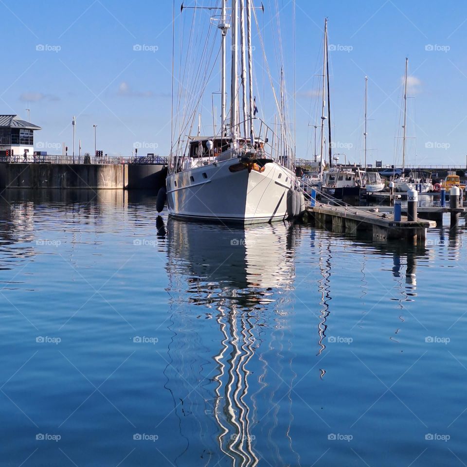 blue sky, boat moored in dock on u.k coast, bright October day. boats reflection on water