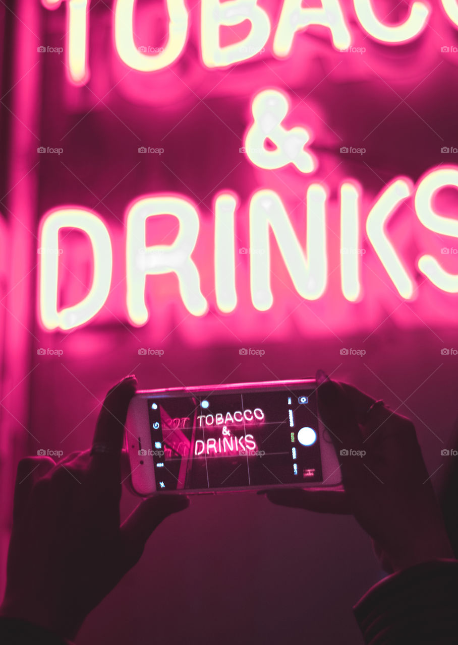 Girl holding a phone to shoot a neon sign.