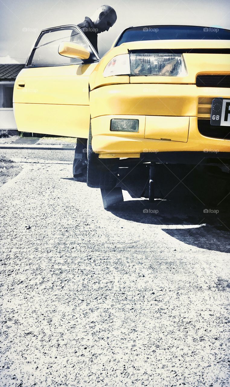 Yellow car on driveway getting repairs.