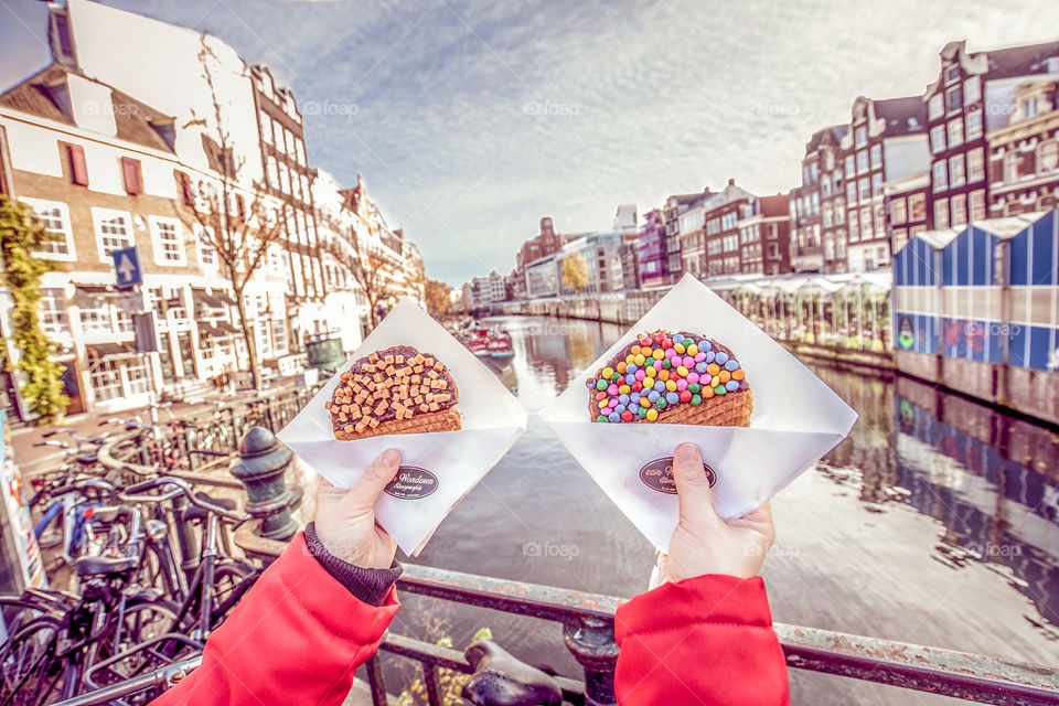 Hands holding traditional stroopwafels biscuits in front of a canal of Amsterdam city in Netherlands.