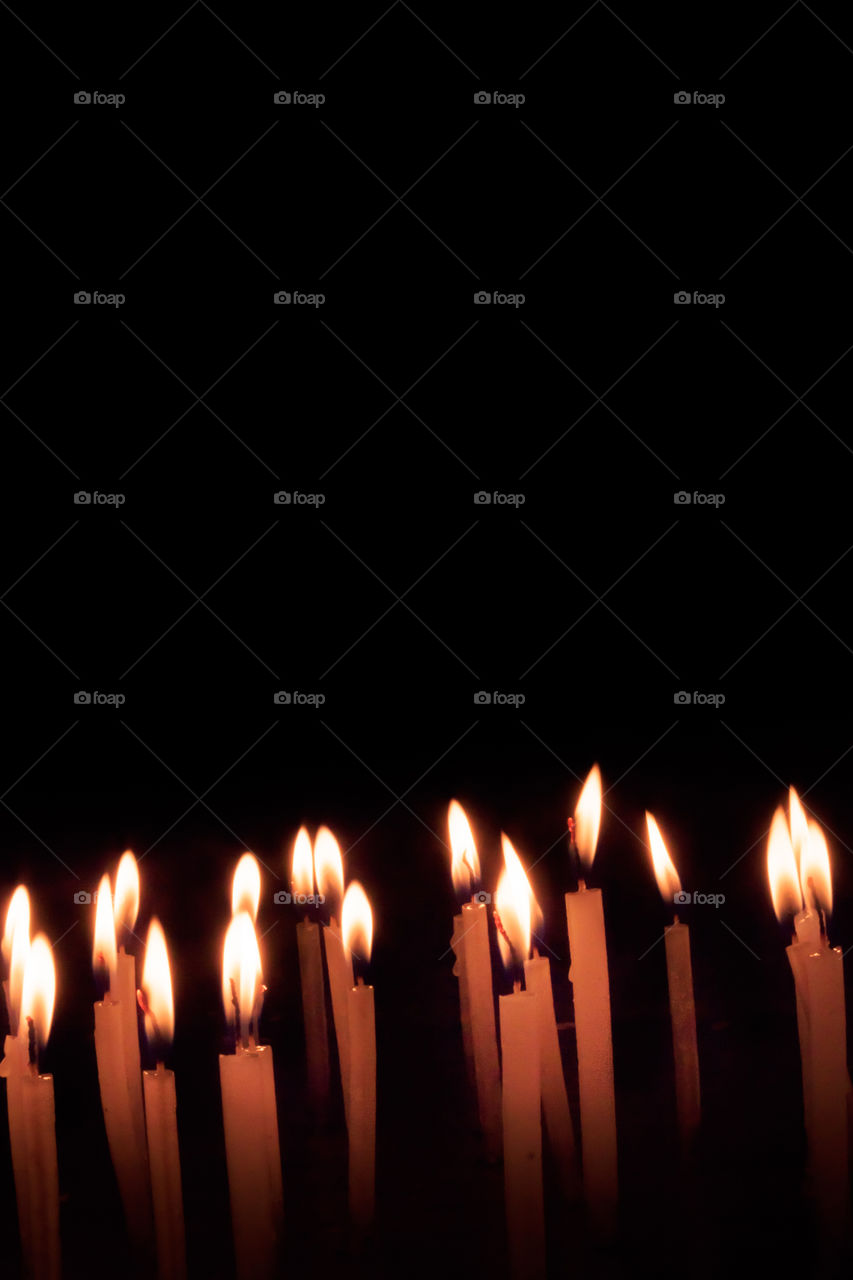 Many Christmas candles burning at night on the black background. Candle flame set isolated in black background. Group of burning candles in dark with shallow depth of field. Close-up. Free space.