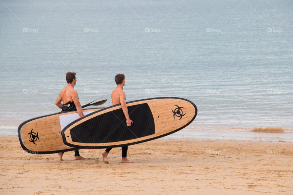 Two people carrying paddleboard on beach