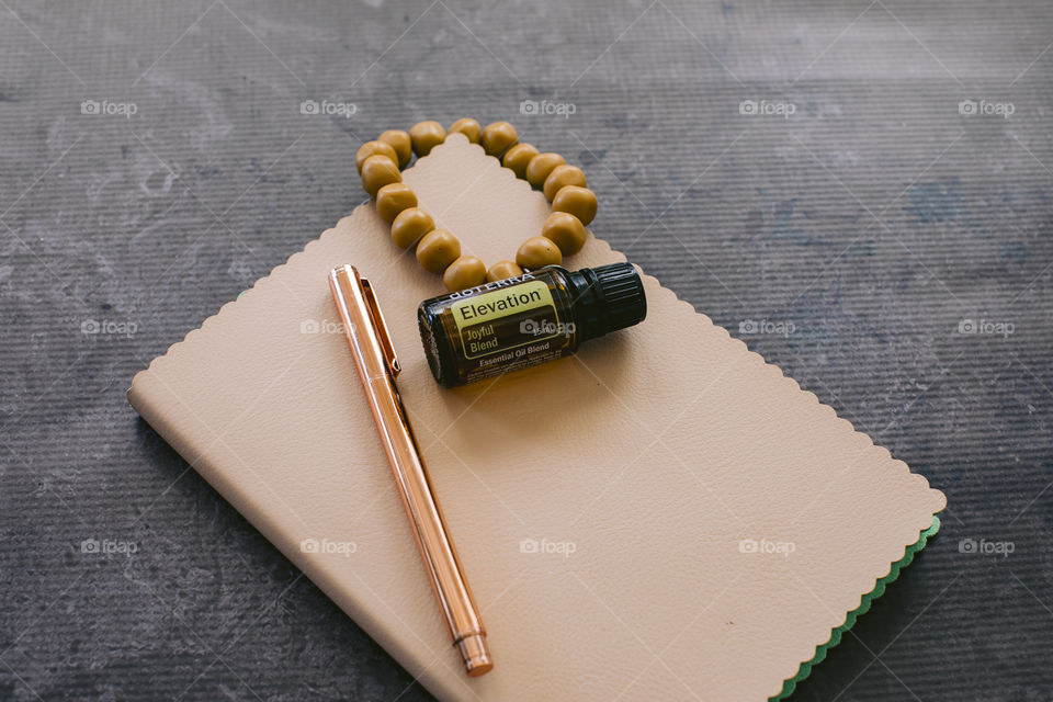 Elevation doterra essential oil bottle on cream notebook with rose gold pen and mustard bead bracelet 