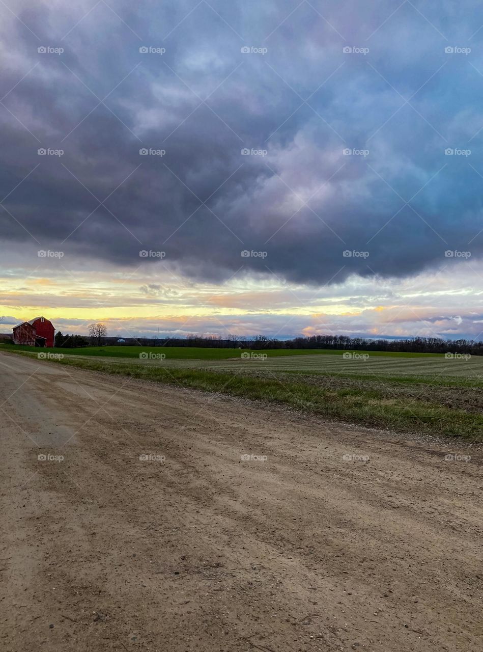 Clouds on a dirt road in Midwest Michigan at sunset where a red barn sits in a green field