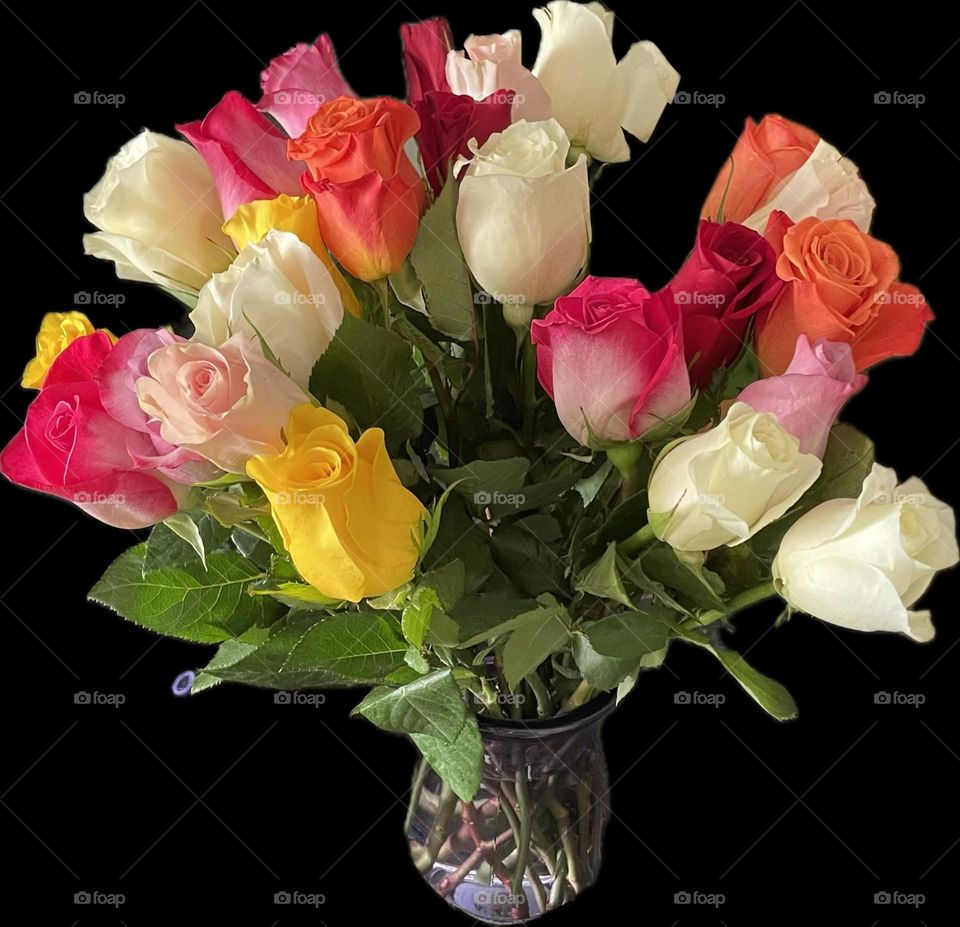 A stunning bouquet of multi-colored roses artfully arranged in a clear glass vase creating a lively display. The flowers include soft white roses, vibrant orange and yellow blooms, deep red petals, delicate pale pink, and bold fuchsia pink roses.