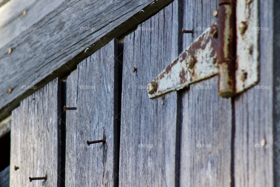 A once-white-painted rusty hinge and rusty nails protruding from random spots on weathered wood siding