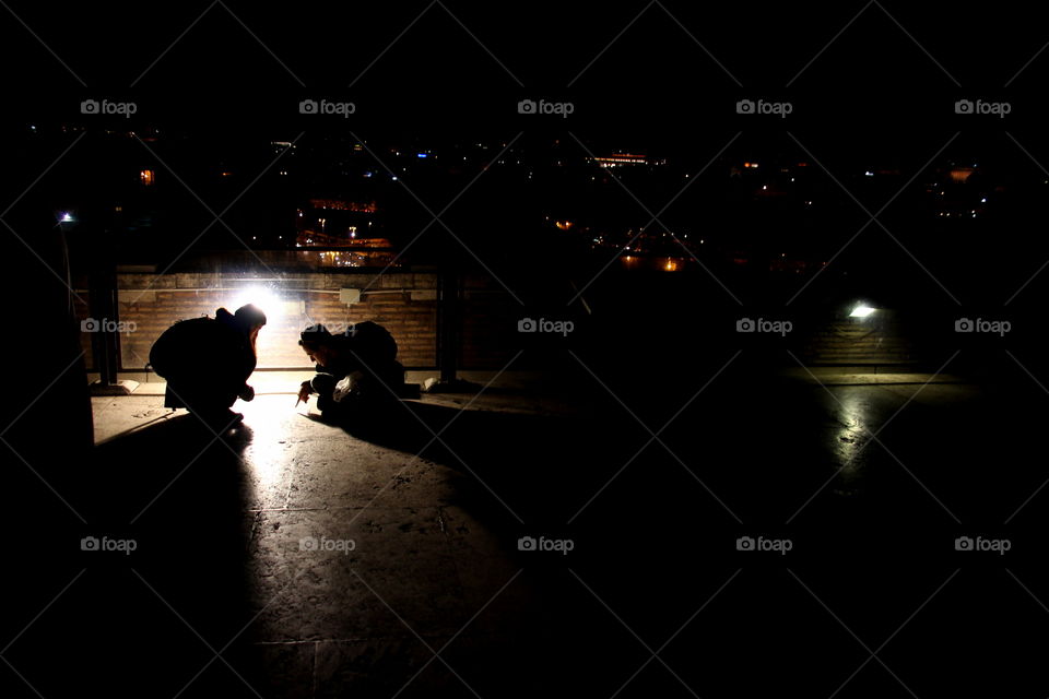 silhouettes of people looking at a map on a roof in the night
